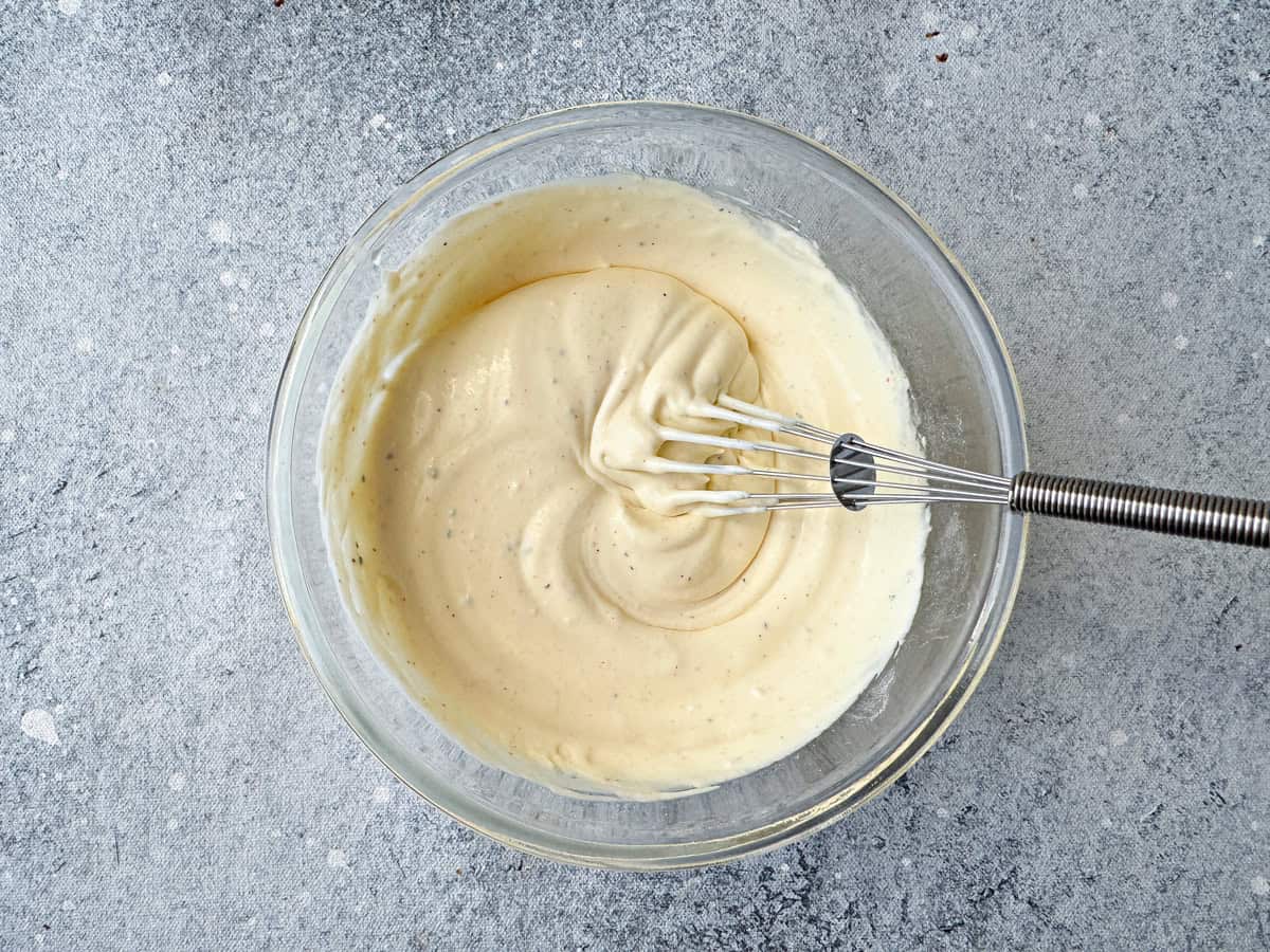 Top-down view of the thoroughly whisked sour cream with seasonings using a whisk in bowl.