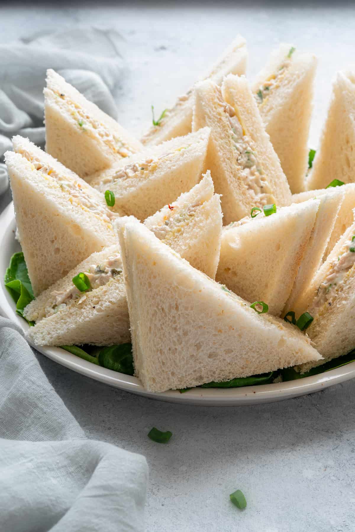 Side close-up view of diagonally cut cold chicken salad sandwiches on a bed of lettuce on a platter, ready to be served!