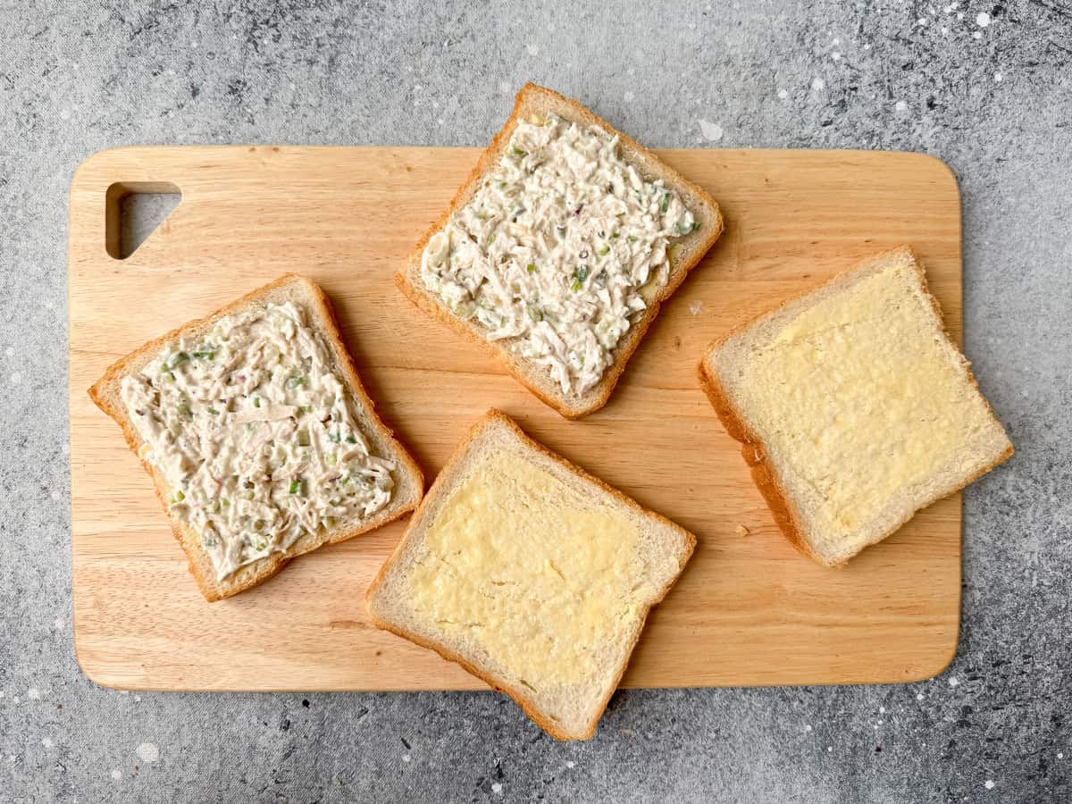 Two out of the four buttered bread slices smeared with the chicken filling.