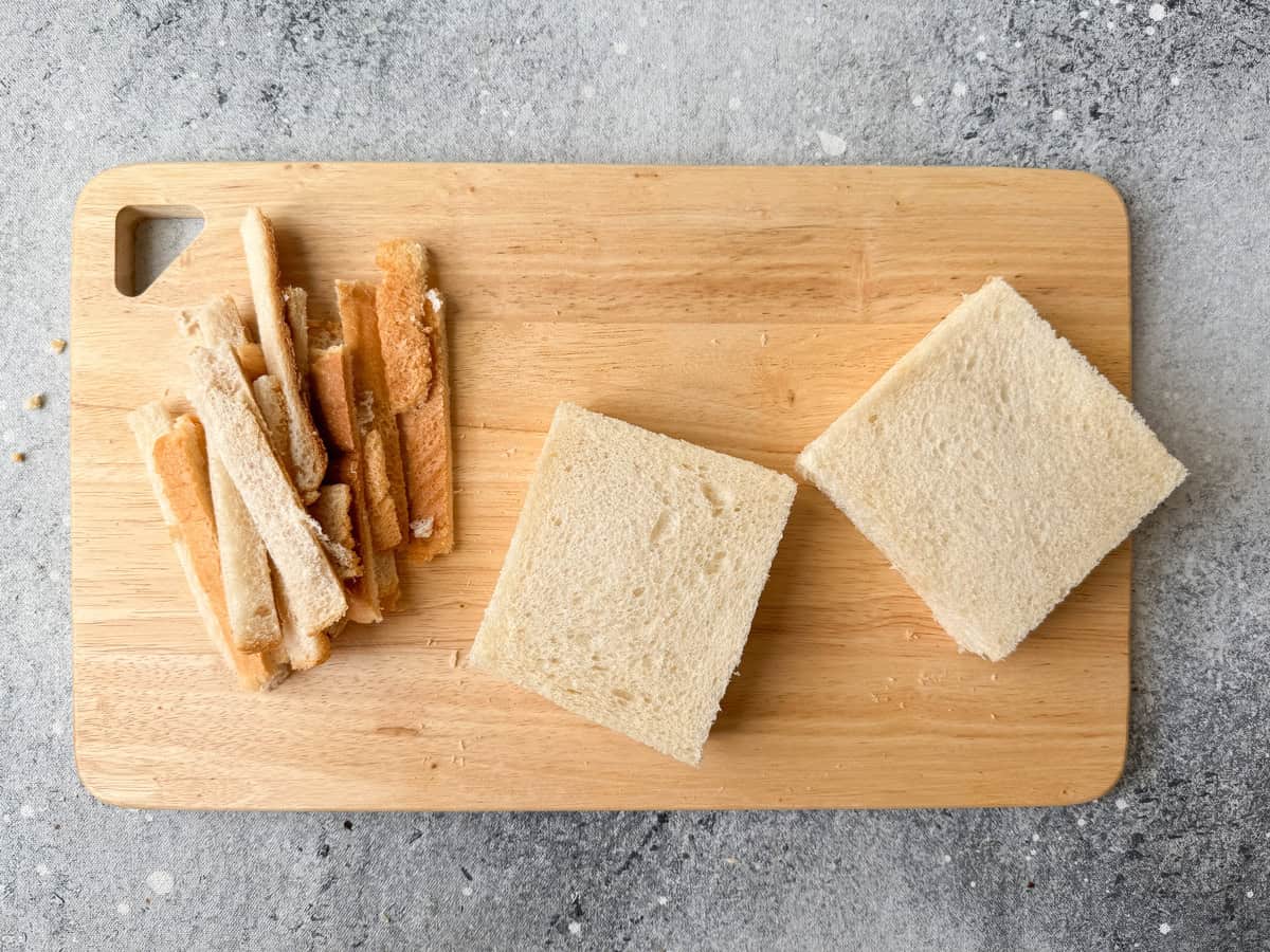 Buttered slices topped on the bread slices smeared with the chicken filling and the edges cut off to remove the crust.