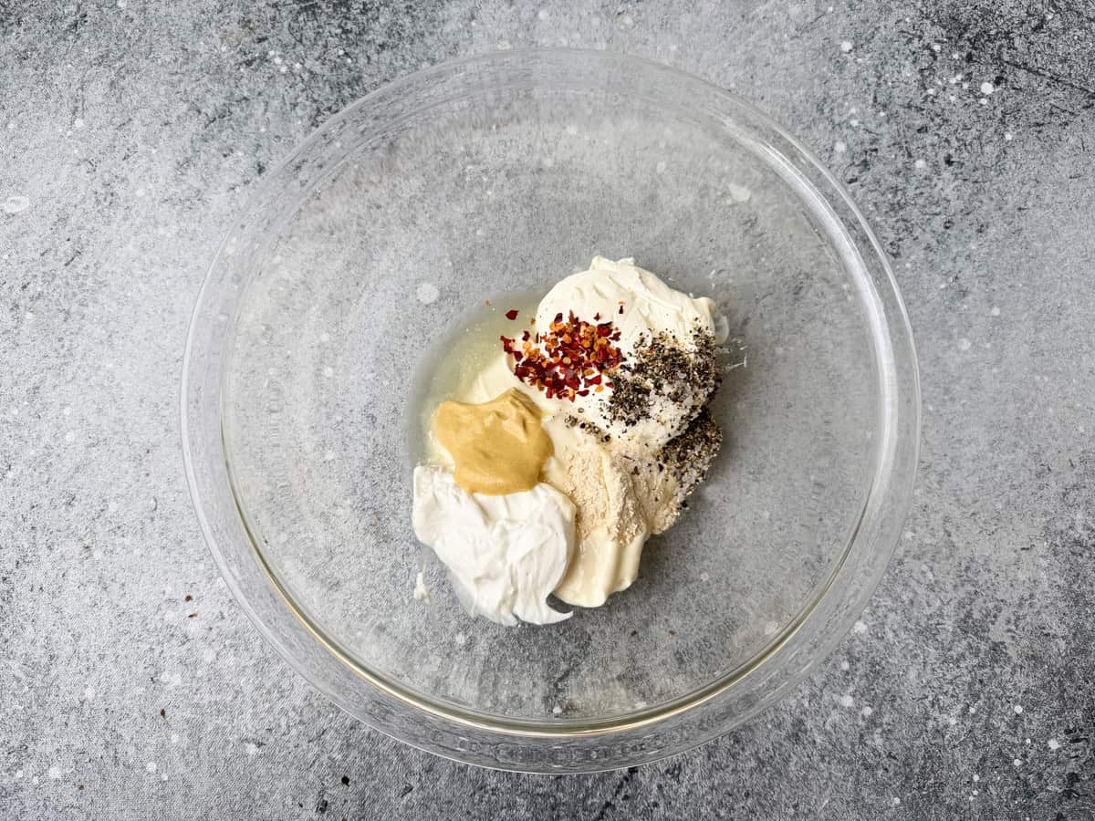Mayonnaise, sour cream, dijon mustard, garlic powder, red pepper flakes, salt, and pepper added to a glass bowl to make creamy dressing.