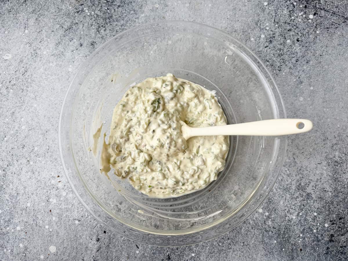 Top-down view of the mayonnaise and sour cream mixture now mixed with pickles, celery, and green onions.