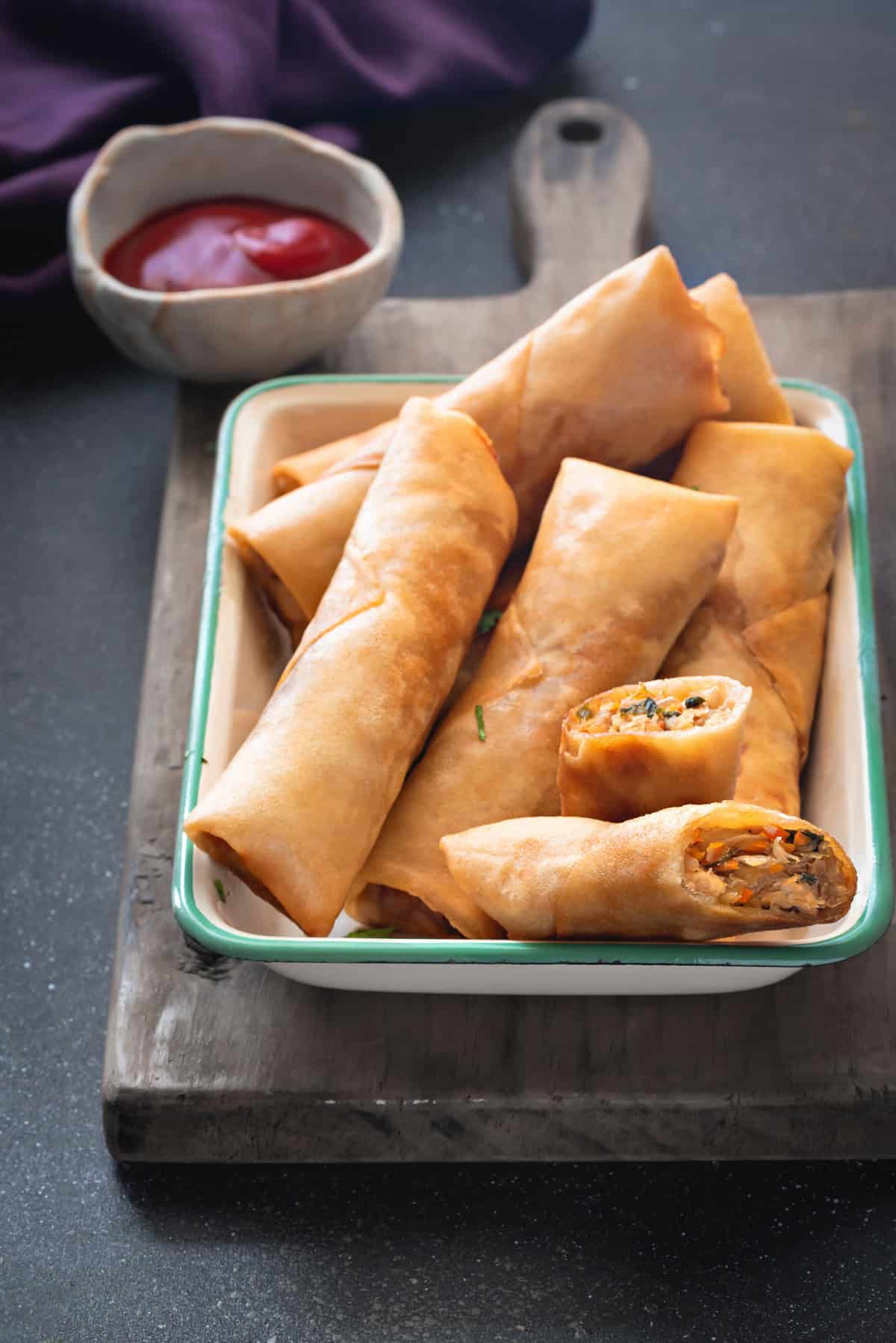 Top-down view of golden fried chicken rolls on a dish with dipping sauce in the background.