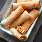 Top-down view of Chicken Spring Rolls in a serving dish with a dipping sauce next to them.