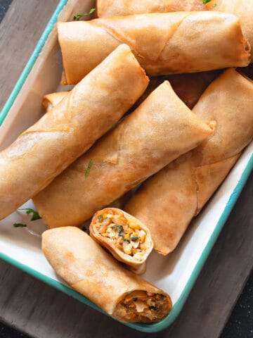 Top-down view of Chicken Spring Rolls in a serving dish with a dipping sauce next to them.