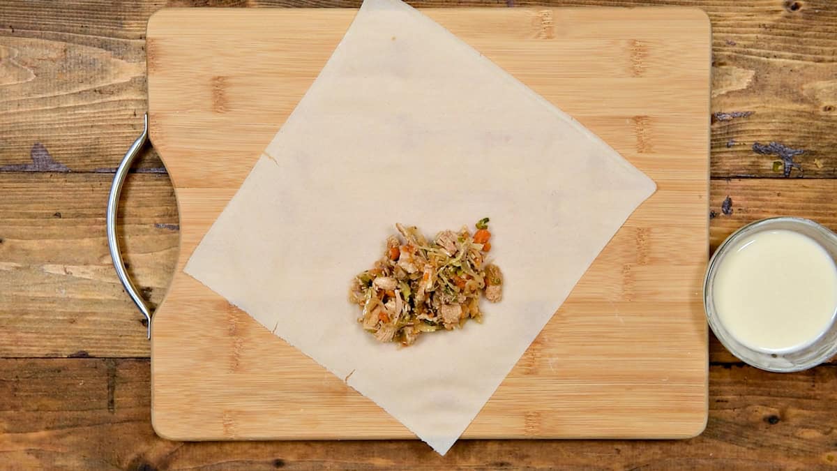 Top-down view of spring roll wrapper with a spoonful of filling laid flat on wooden board.