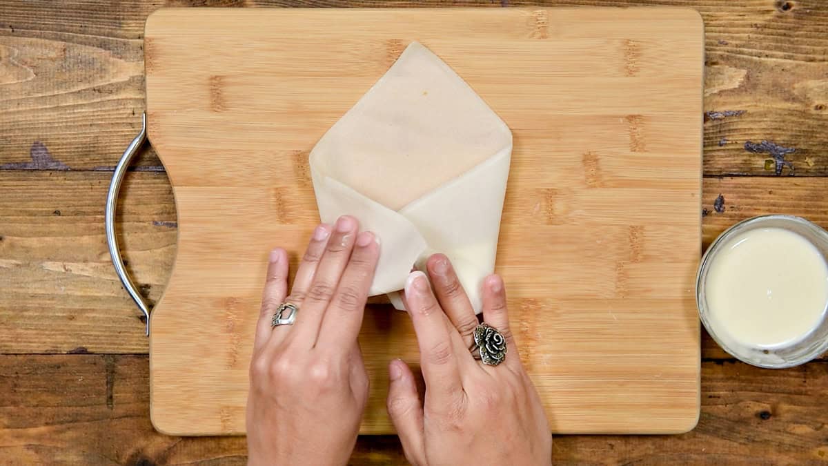 Top-down view of Chinese chicken roll wrapped over the first roll with a shape resembling like an envelope before final wrap.