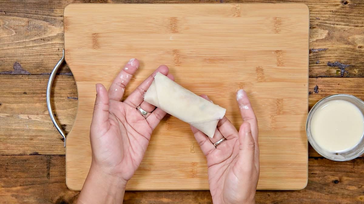 Top-down view of hands holding fully sealed Chinese chicken roll ready to be fried.