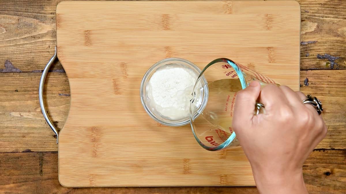 Top-down view of flour and water added to a bowl to create a paste for sealing the Chinese chicken rolls.