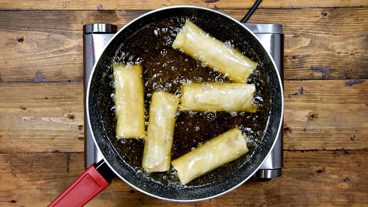Top-down view of a pan with oil that is frying the spring rolls.