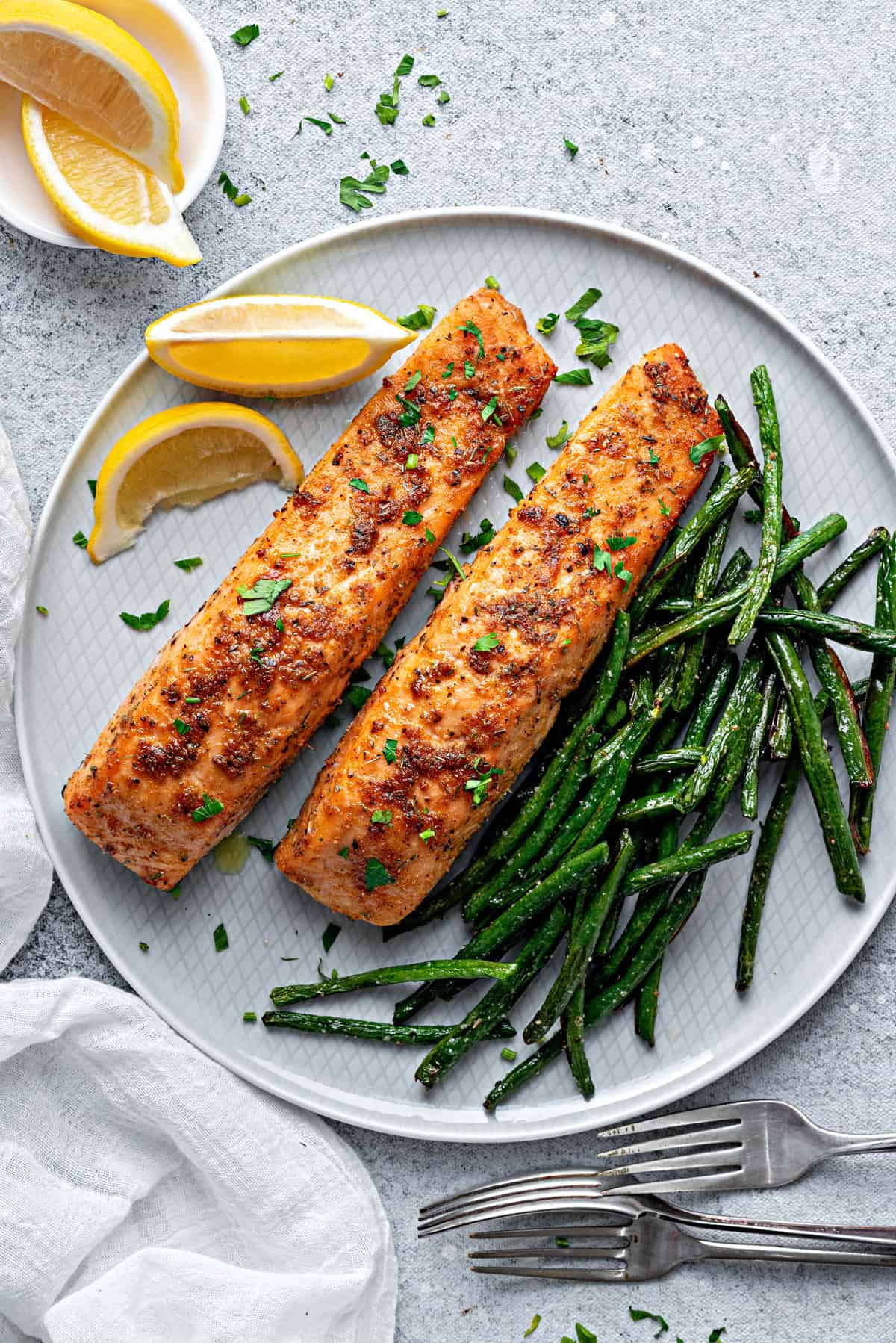 Salmon filets on a plate with green beans and lemon garnish that have been air-fried and are ready to be served.