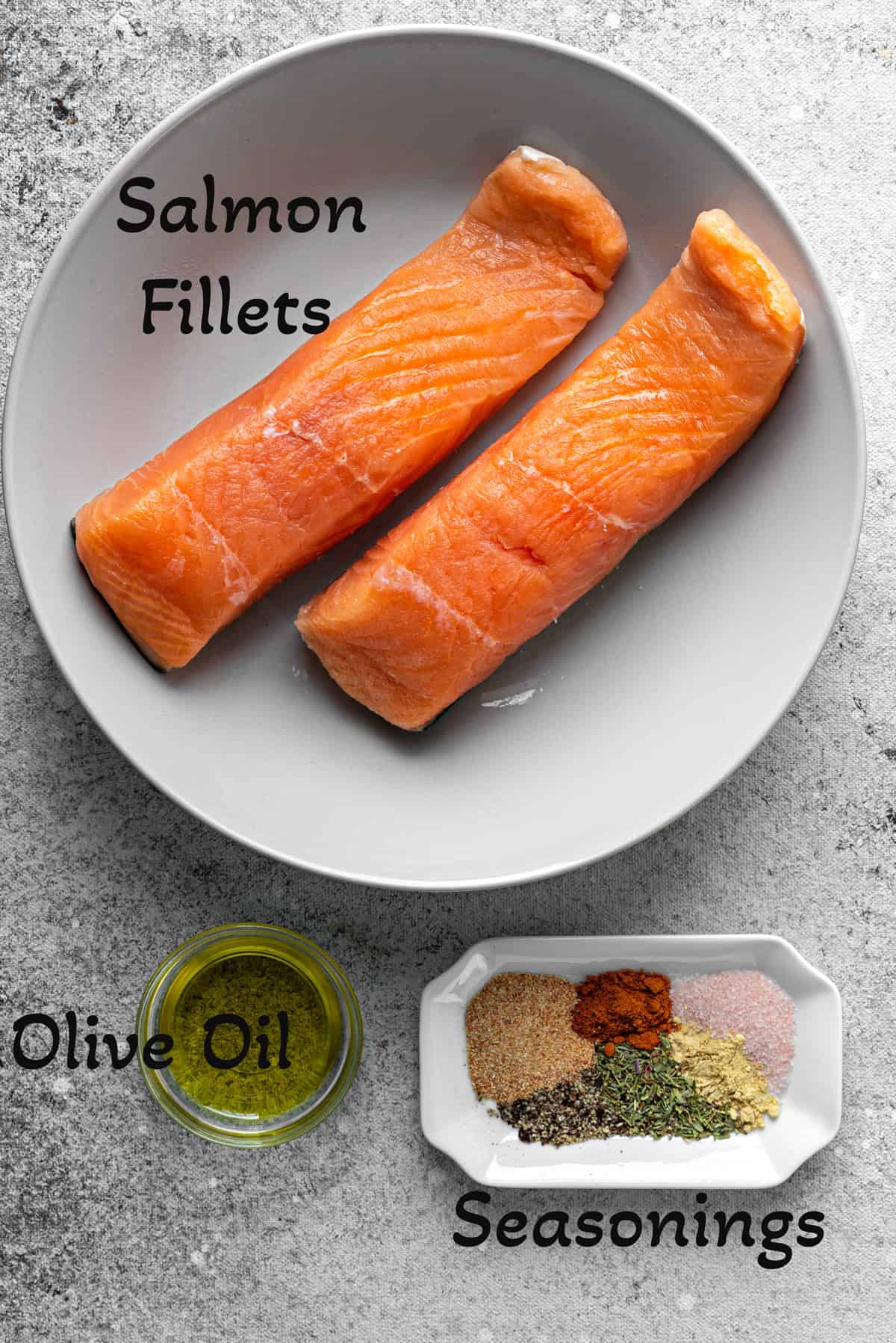 Top-down view of raw salmon filets on a plate, a small bowl of olive oil, and a small plate of seasonings like salt, pepper, garlic powder, and dried thyme.