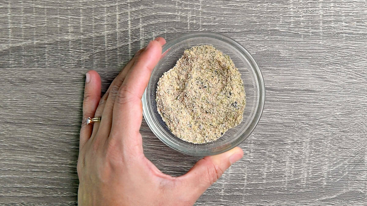 A hand holding a glass bowl with seasonings that's been mixed together.