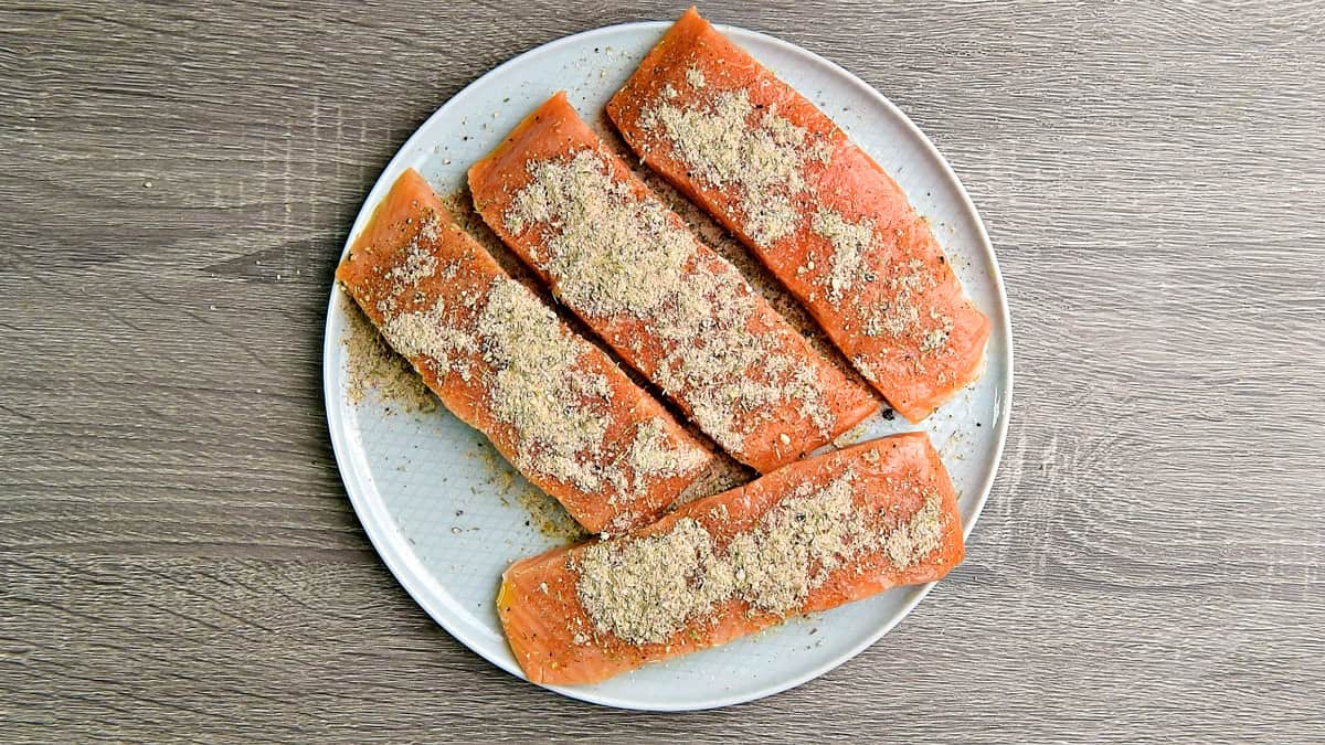 Salmon filets on a plate that have been coated with olive now coated with the spice mixture.