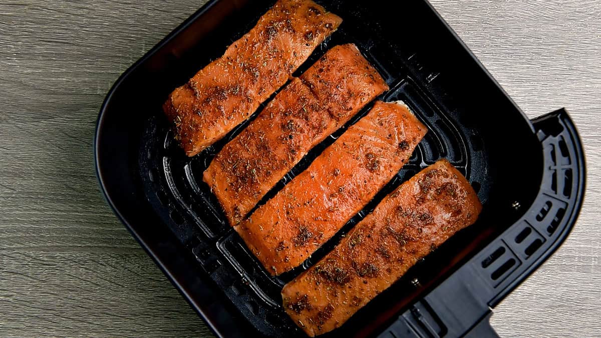 Top-down view of salmon fillets in an air fryer, evenly spaced and not touching each other.