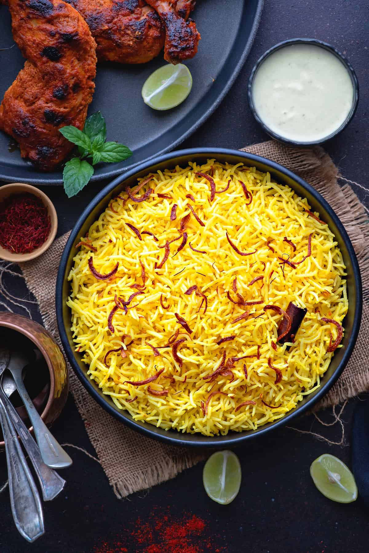 Above-view of Saffron Rice fluffed and ready to serve, topped with saffron, cinnamon stick, and paired with Chicken and a creamy dip.