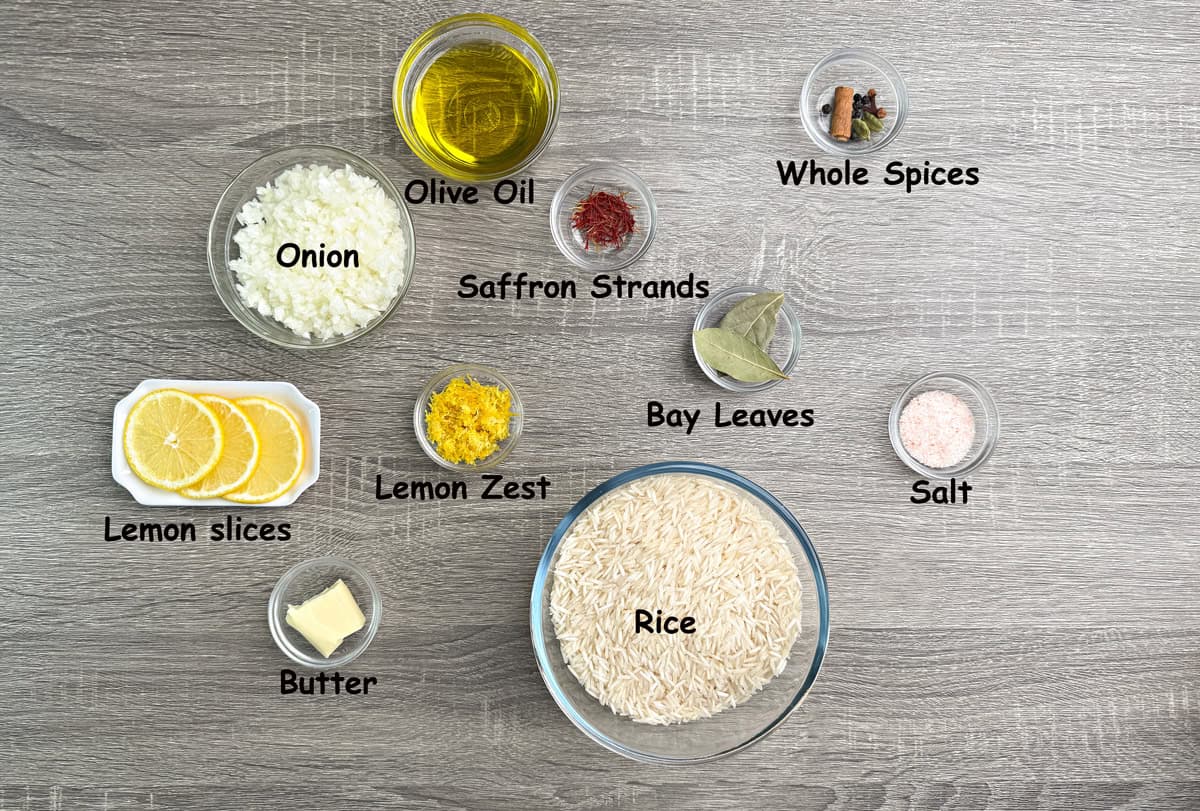 Recipe ingredients that include aged basmati rice, saffron strands, olive oil and butter, spices, diced onion, and lemon in individual glass bowls