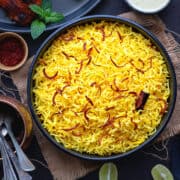 Saffron Rice fluffed and ready to serve, topped with saffron, cinnamon stick, and paired with Chicken and a creamy dip.