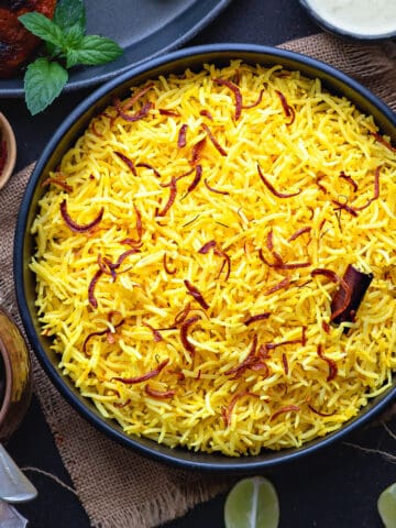 Saffron Rice fluffed and ready to serve, topped with saffron, cinnamon stick, and paired with Chicken and a creamy dip.