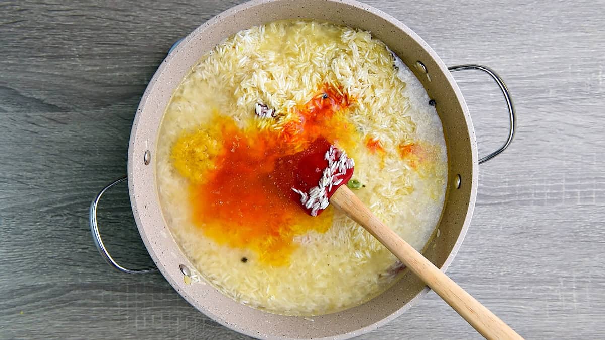 Top-down view of water, salt, lemon zest, and bloomed saffron water added being added to the toasted rice mixture in the skillet.