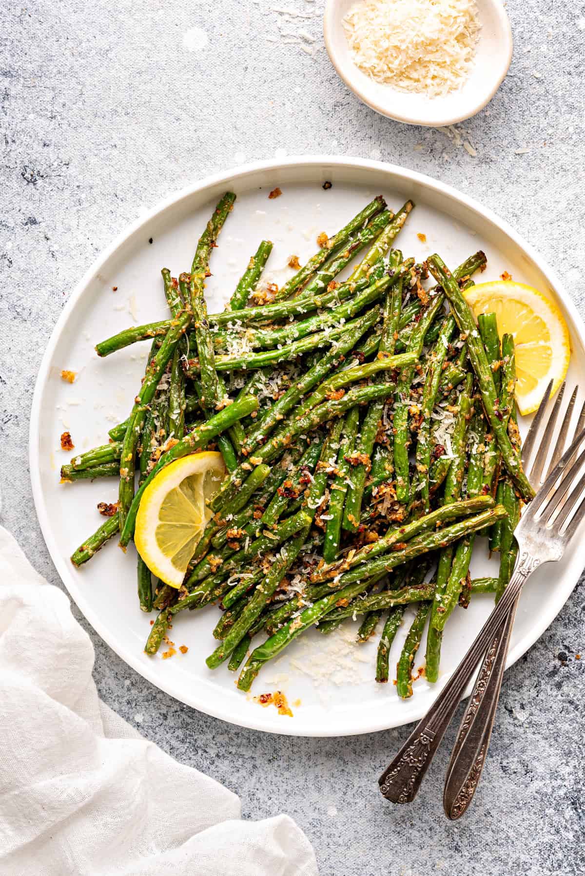Top-down view of green beans that have been roasted in an air fryer topped with parmesan cheese, garlic powder, and lemons.