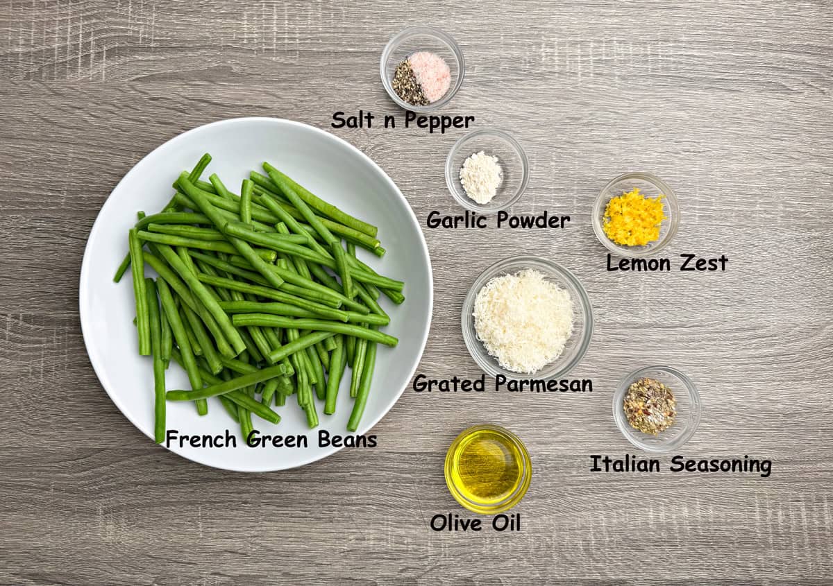 Recipe ingredients in individual glass bowls that include haricot vert beans, grated parmesan, Italian seasoning, olive oil, lemon zest, and garlic powder.