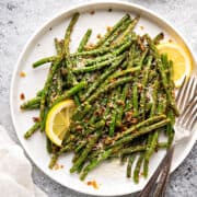 Air fryer green beans served on a white ceramic plate, and topped with parmesan cheese, garlic powder, and lemons.