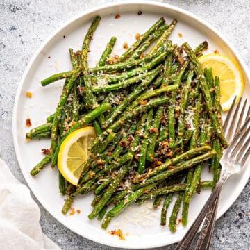 Air fryer green beans served on a white ceramic plate, and topped with parmesan cheese, garlic powder, and lemons.