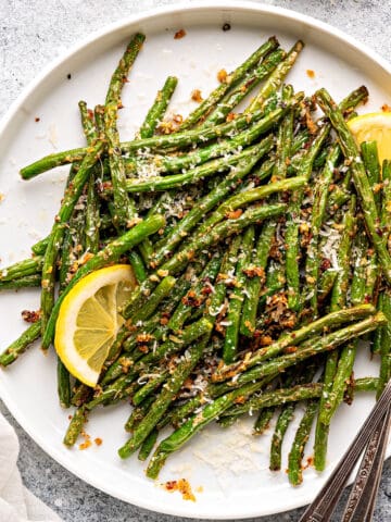 Air fryer green beans served on a white ceramic plate, and topped with parmesan cheese, garlic powder, and lemons.