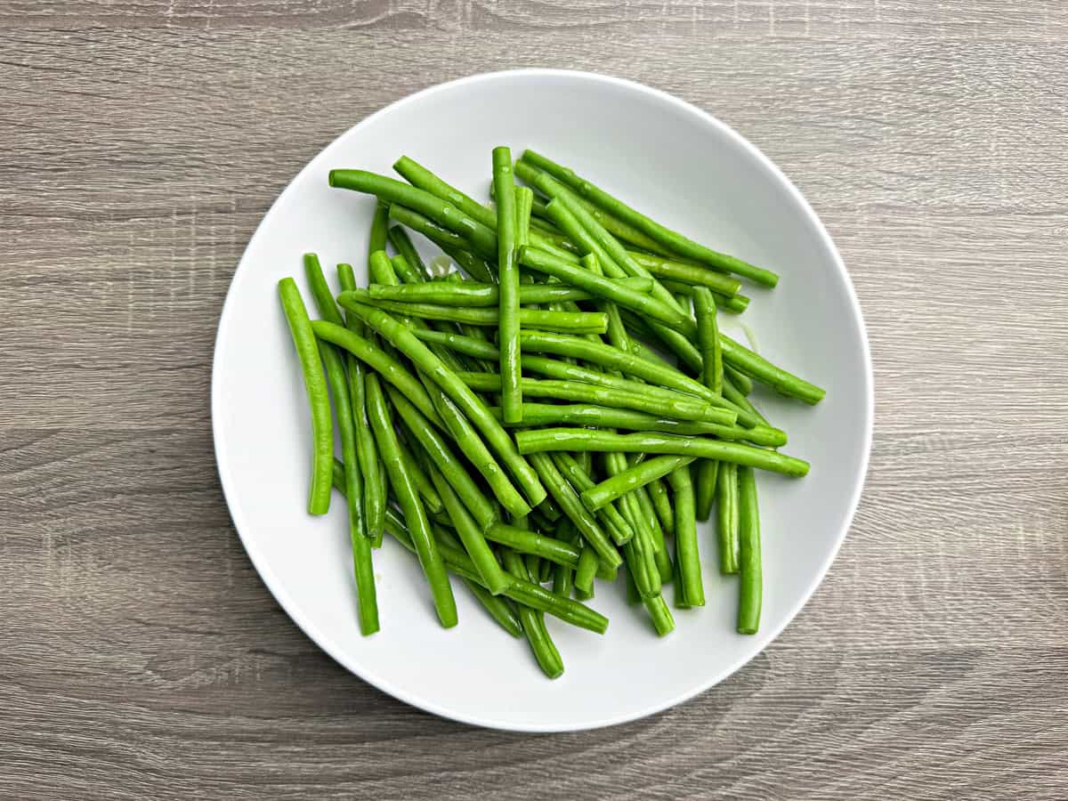 A view of french green beans in a bowl that have been washed and dried, and coated with olive oil.