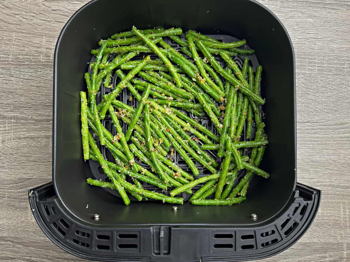The green beans that have been coated with their seasonings now placed evenly and not over crowded in an air fryer basket.