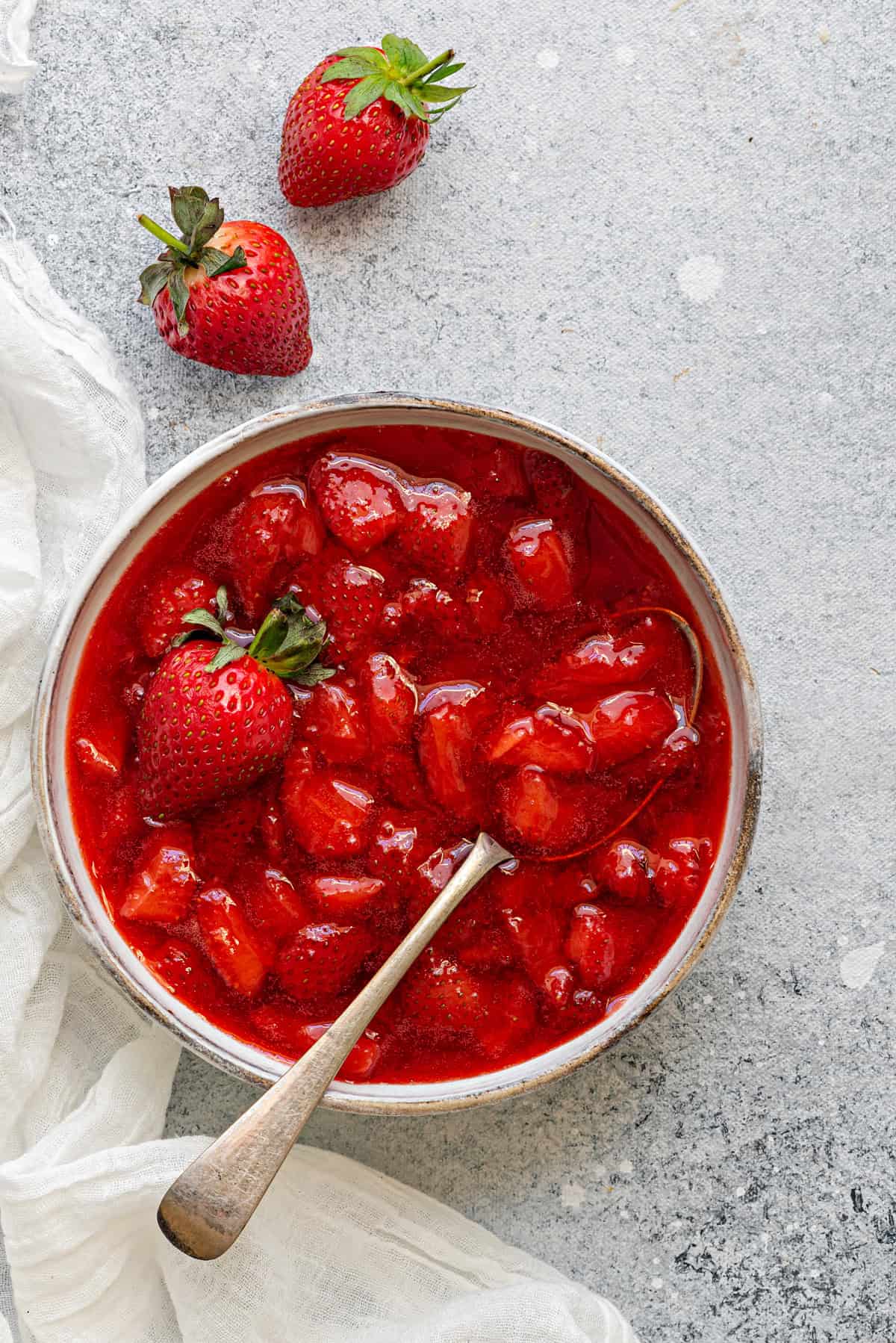 Top-down view of compote style Strawberry sauce inside a bowl with a spoon ready to be used as a topping.