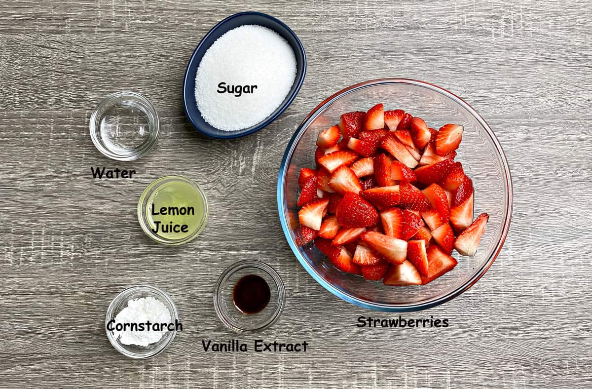 Top-down view of sauce recipe ingredients placed in the individual glass bowls that include fresh strawberries cornstarch, vanilla extract, lemon juice, water, and sugar in a bowl.