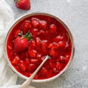 Top-down view of compote style Strawberry sauce inside a white bowl with a spoon ready to be used as a topping.