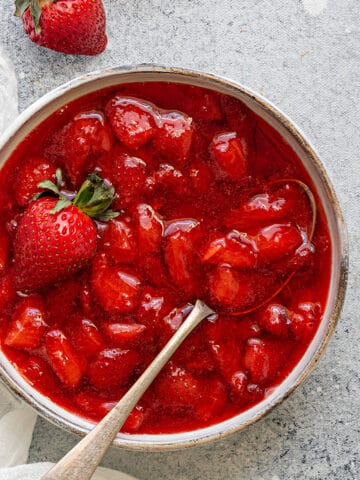 Top-down view of compote style Strawberry sauce inside a white bowl with a spoon ready to be used as a topping.