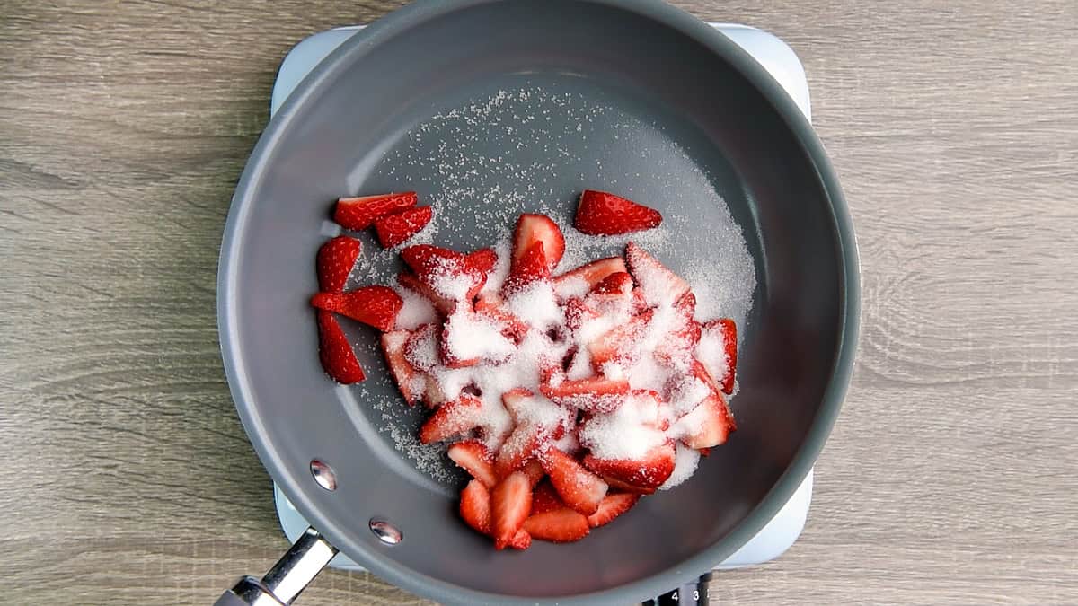Fresh strawberries and sugar added to a pan.