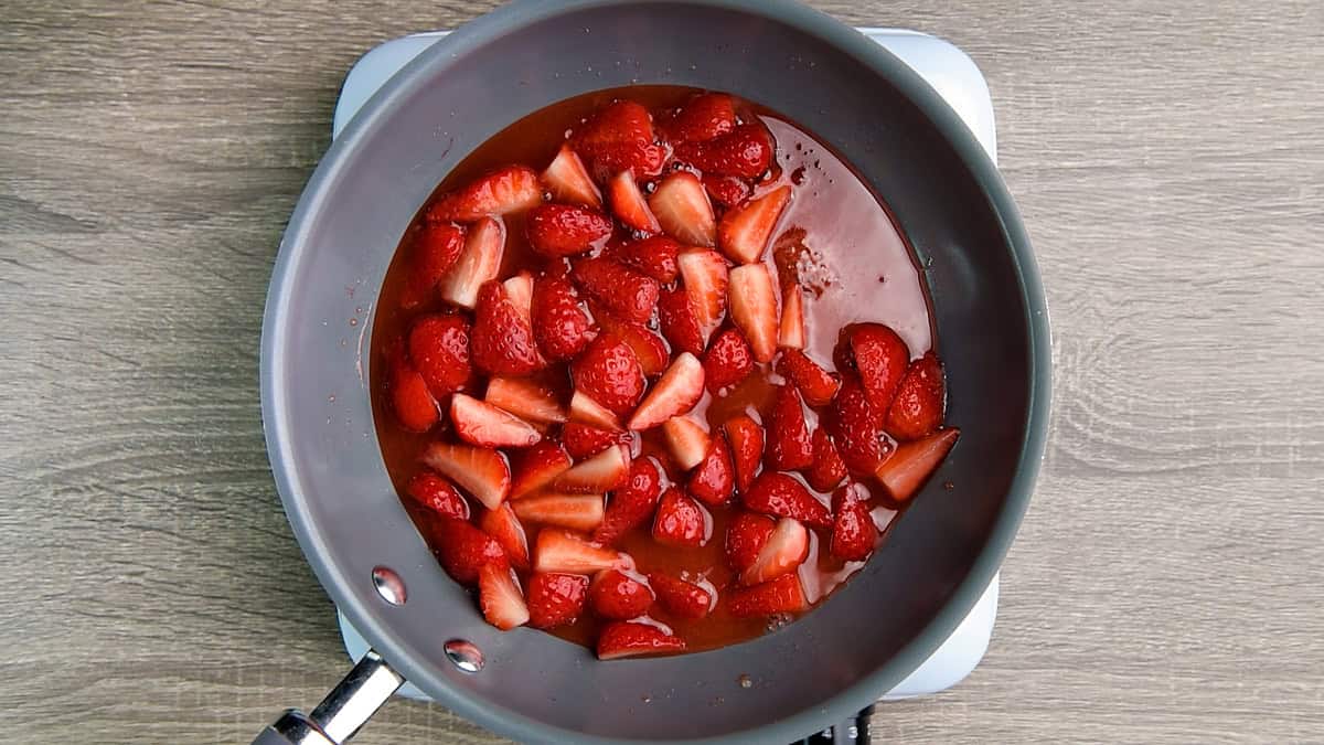 Strawberries simmering in sugar and cornstarch mixture in the pan.