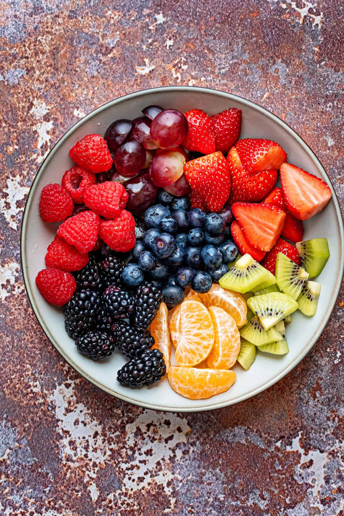 Assorted fruit of strawberries, grapes, raspberries, kiwi, blueberries, blackberries, mandarin oranges, for berry fruit salad inside a bowl.