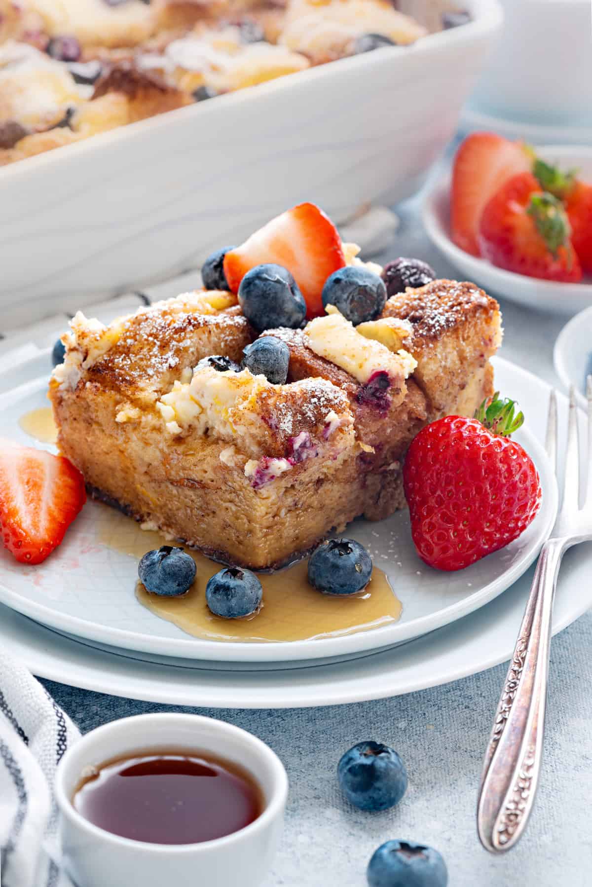 Top-down view of overnight French toast Casserole topped with fresh blueberries and strawberries and drizzled with syrup.