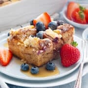 Top-down view of overnight French toast Casserole topped with, lemony cream cheese, fresh blueberries and strawberries and drizzled with syrup.