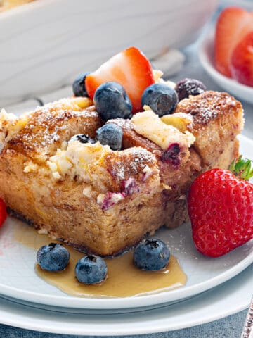 Top-down view of overnight French toast Casserole topped with, lemony cream cheese, fresh blueberries and strawberries and drizzled with syrup.