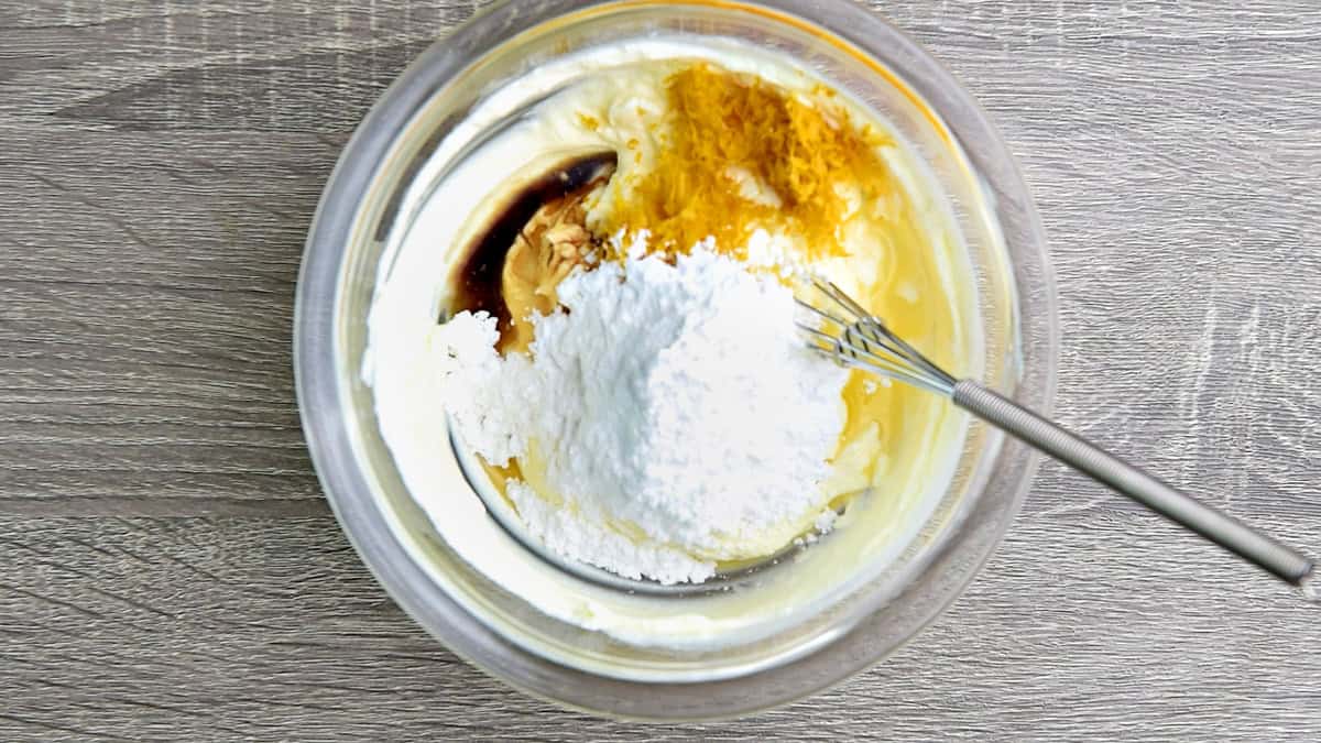 The lemon zest, lemon juice, vanilla extract, and confectioner sugar added to the bowl that has smooth cream cheese.