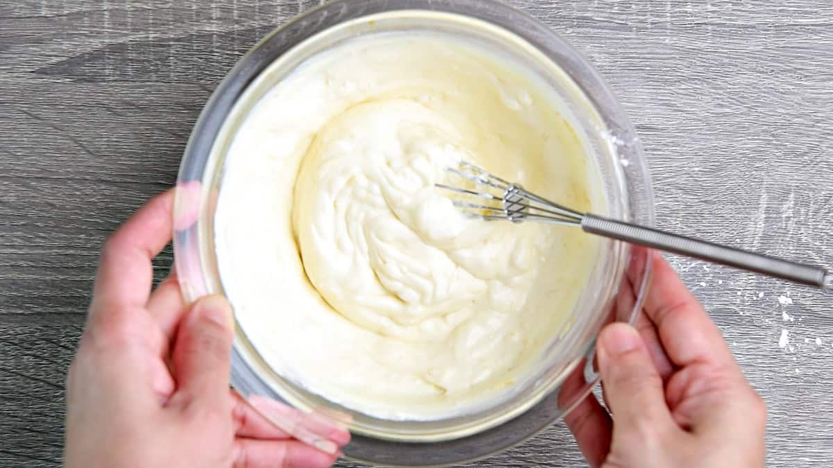 Hands holding the bowl of creamy cheesecake mixture, ready to use for topping.