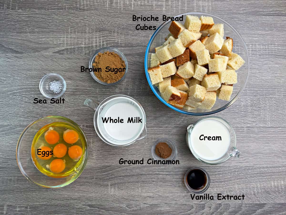 Ingredients for casserole base of French toast that includes cubes brioche bread, brown sugar, whole milk, cream, eggs, vanilla extract and sea salt.
