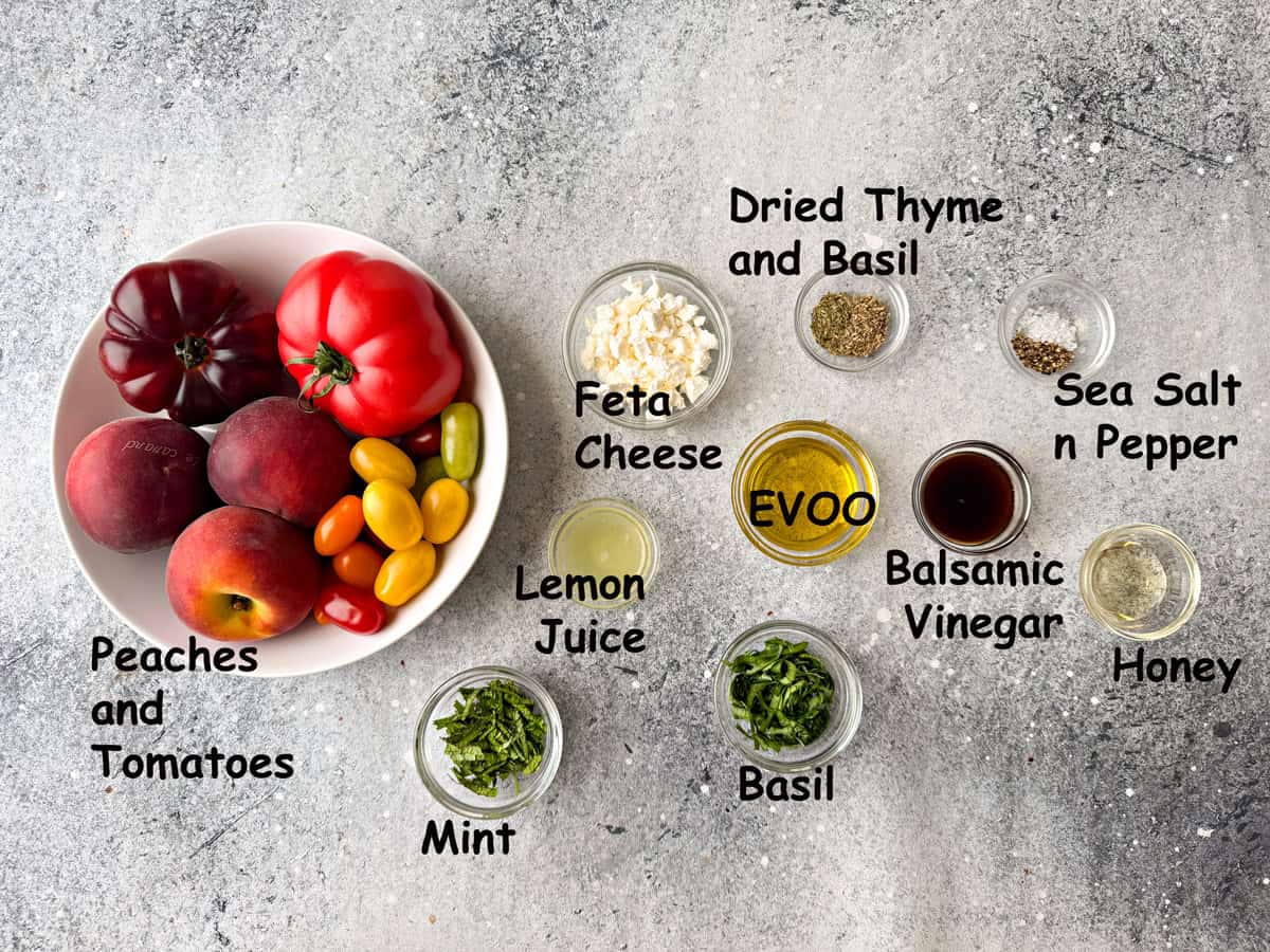 Recipe ingredients for tomato and peach salad that are all in bowls that include tomatoes, lemon juice, mint, basil, feta, balsamic vinegar, and more.