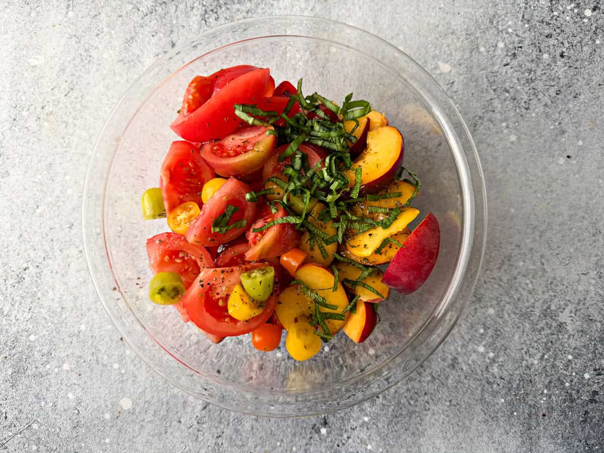 Tomatoes, Peaches, fresh mint and basil herbs placed in a large bowl with salt and freshly ground pepper.