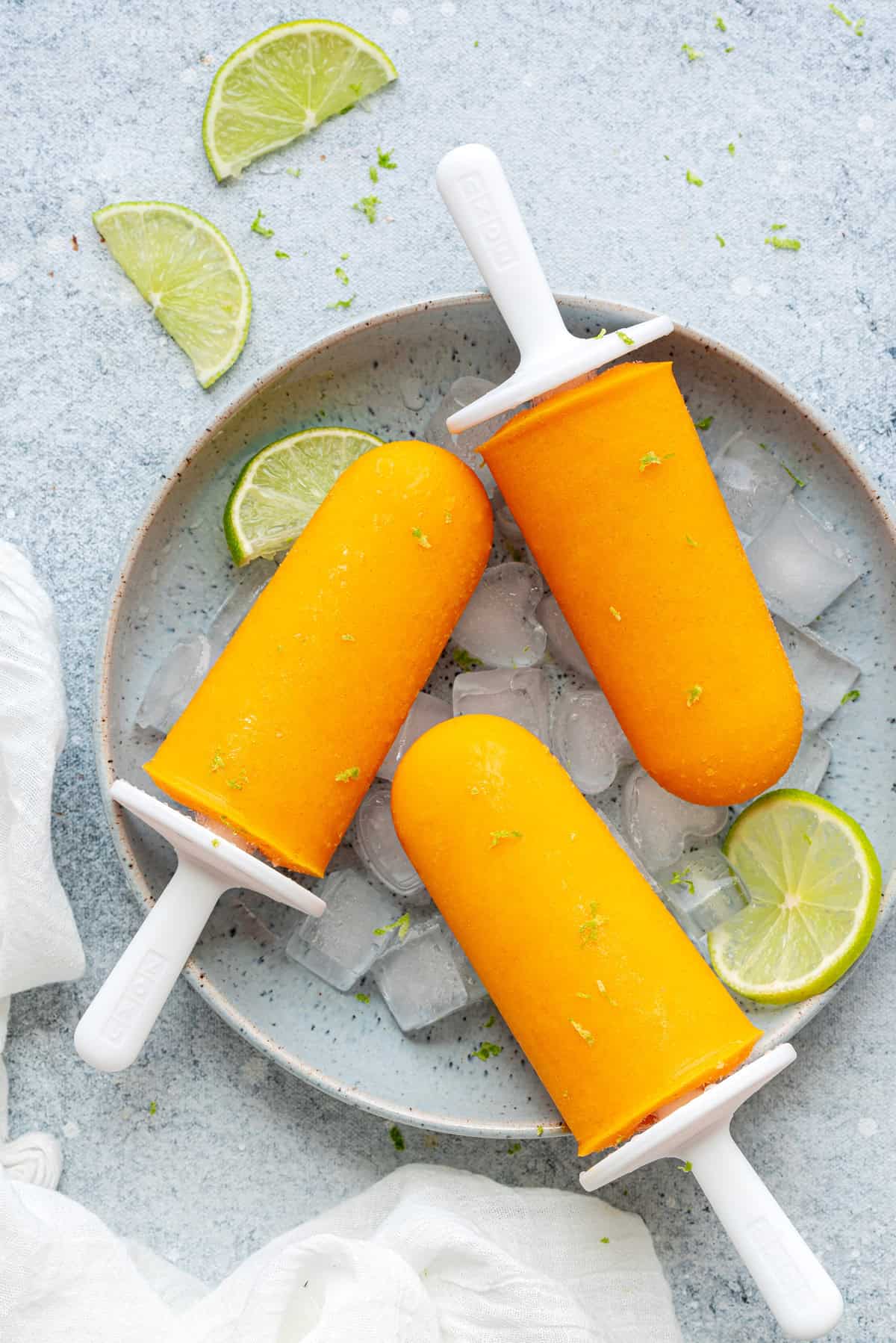 Top-down view of Mango popsicles in a bowl on ice with limes and lime zest shavings on the popsicles.