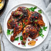 Middle Eastern flavored spatchcock chicken served on white earthen plate with roasted veggies on side in a cast iron pan.