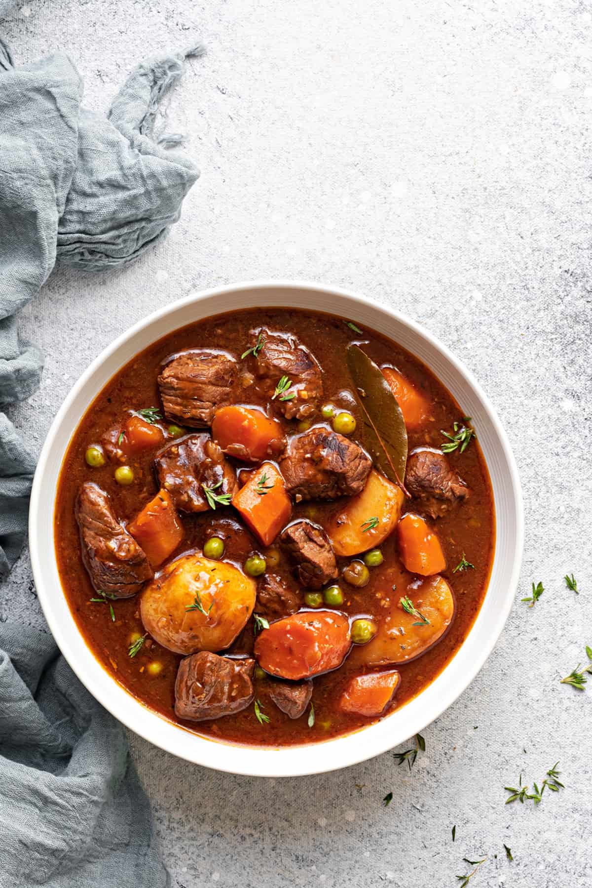 A white bowl of instant pot beef stew meat and gravy with potatoes, carrots and peas.