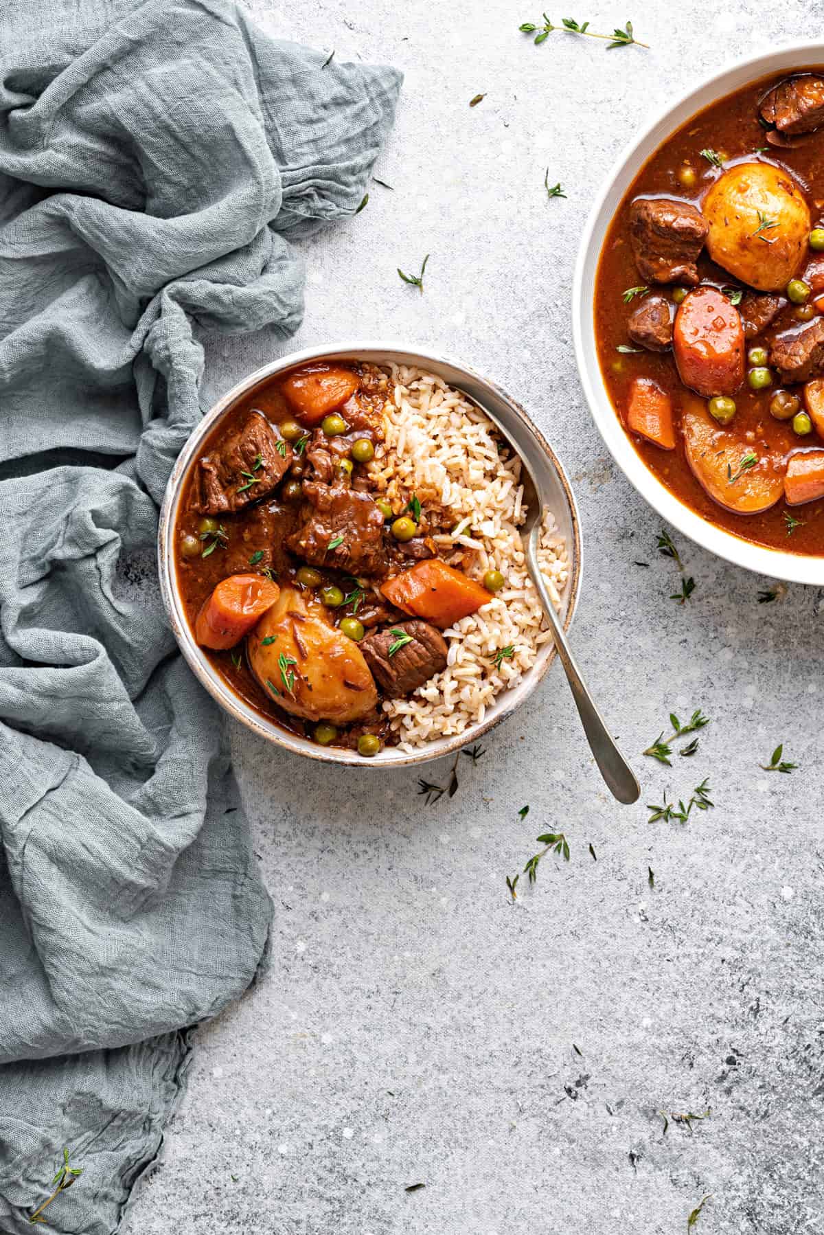 A bowl of beef stew gravy with brown rice and a spoon. Stew in serving bowl on side.